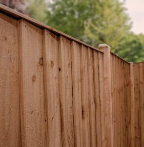 A wooden privacy fence with vertical boards and posts extending into the distance, with green trees in the background.