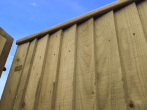 Close-up of vertical wooden fence panels with nails under a blue sky.