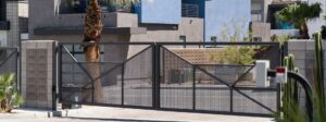 A modern black metal gate with X-shaped crossbars spans a driveway behind gray stone walls.