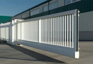 White metal gate and fence along a concrete driveway beside an industrial building.