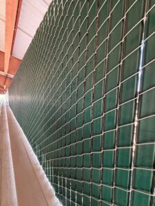 Side view of a green metal fence with a square-grid pattern along a walkway.