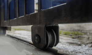 Close-up of a metal gate's bottom wheel and bracket on a wet sidewalk.