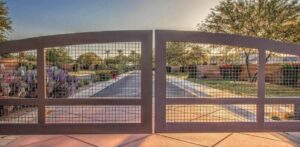 A wooden gate with metal grid panels opens onto a sunlit garden path lined with trees.