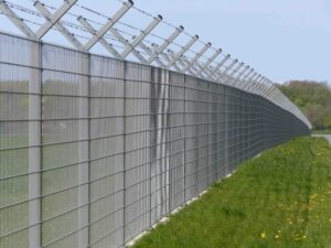 A long curved metal security fence with barbed wire along a grassy area.