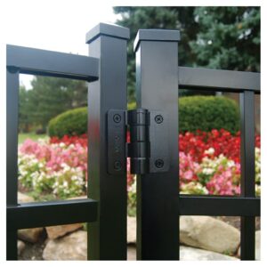 Close-up of a black metal gate hinge on a fence with colorful garden flowers in the background.