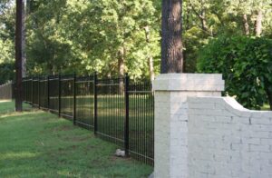 A black metal fence runs along a grassy lawn beside a white brick wall, with trees in the background.