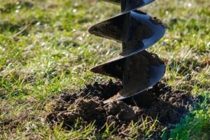 Close-up of a metal auger partially buried in soil on a grassy area.