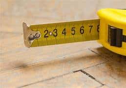 Close-up of a yellow tape measure extended on a wooden floor, with numbers 2 through 7 visible.