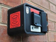 Small black electrical box with a red label mounted on a brick wall.