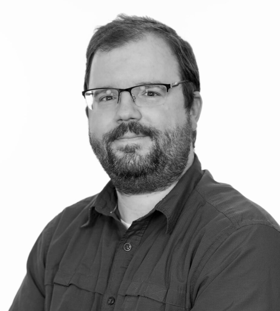 Portrait of a bearded man wearing glasses and a dark button-up shirt.