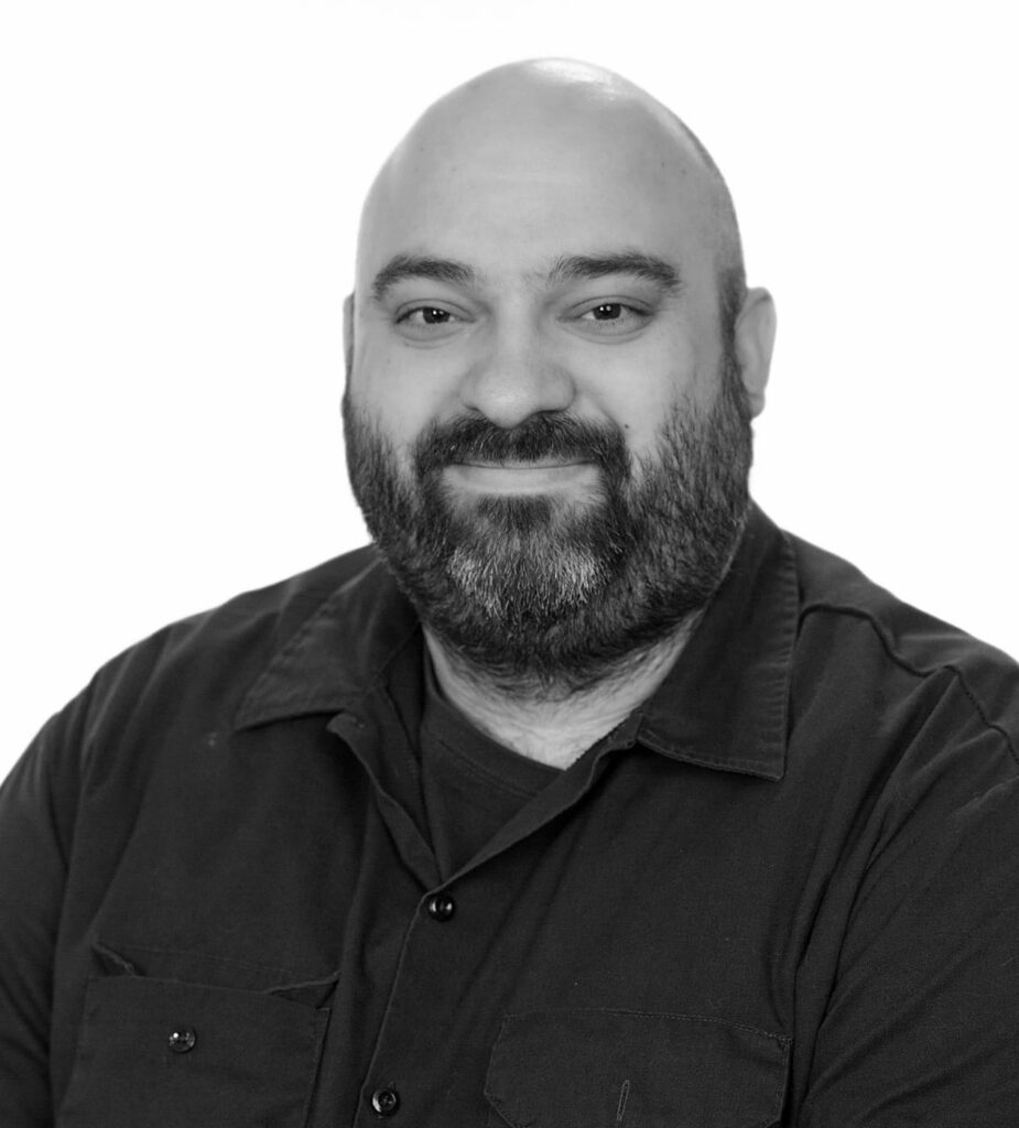 Black-and-white portrait of a bald man with a beard wearing a dark shirt and smiling.