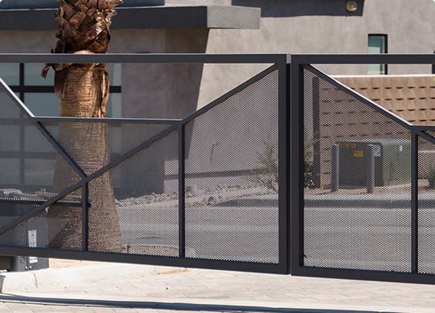 A modern black metal gate with glass panels and diagonal supports sits in front of a beige building with a palm tree behind it.