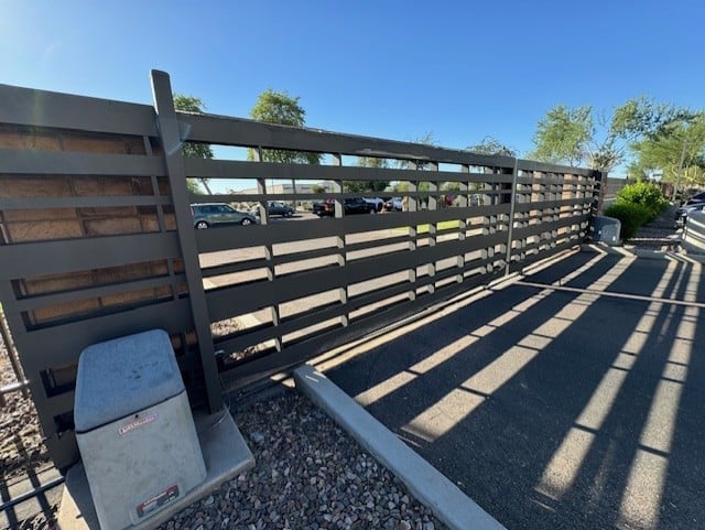 A wooden horizontal slat fence runs along a paved walkway, casting striped shadows on the ground.